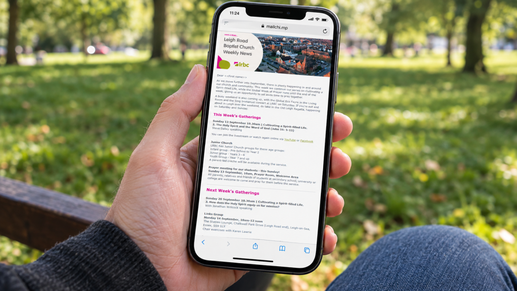 A hand holding a smartphone showing the LRBC email newsletter on the screen. With grass an parkland behind.